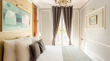 A hotel room with a large bed, a chandelier, a painting, and a window with curtains.