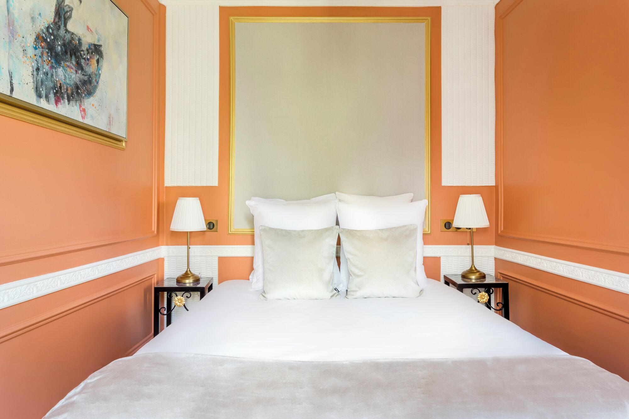 Un cuarto de hotel con una cama grande, ropa de cama blanca, dos mesitas de noche con lámparas y un cuadro en la pared.