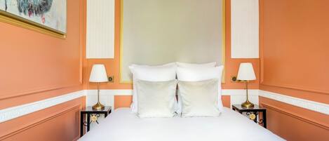 Un cuarto de hotel con una cama grande, ropa de cama blanca, dos mesitas de noche con lámparas y un cuadro en la pared.