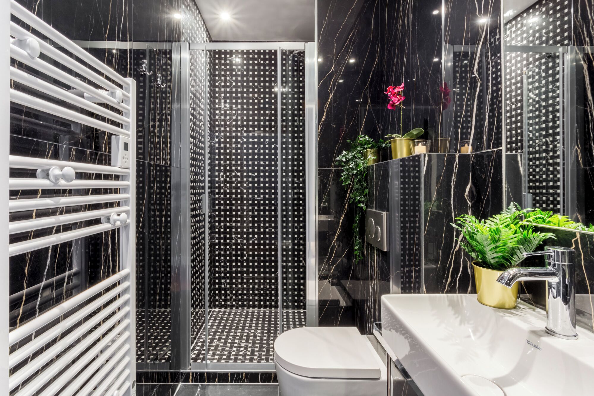 Ein modernes Badezimmer mit Duschkabine aus Glas, einer weißen Toilette und einem Waschbecken mit goldfarbenem Wasserhahn.