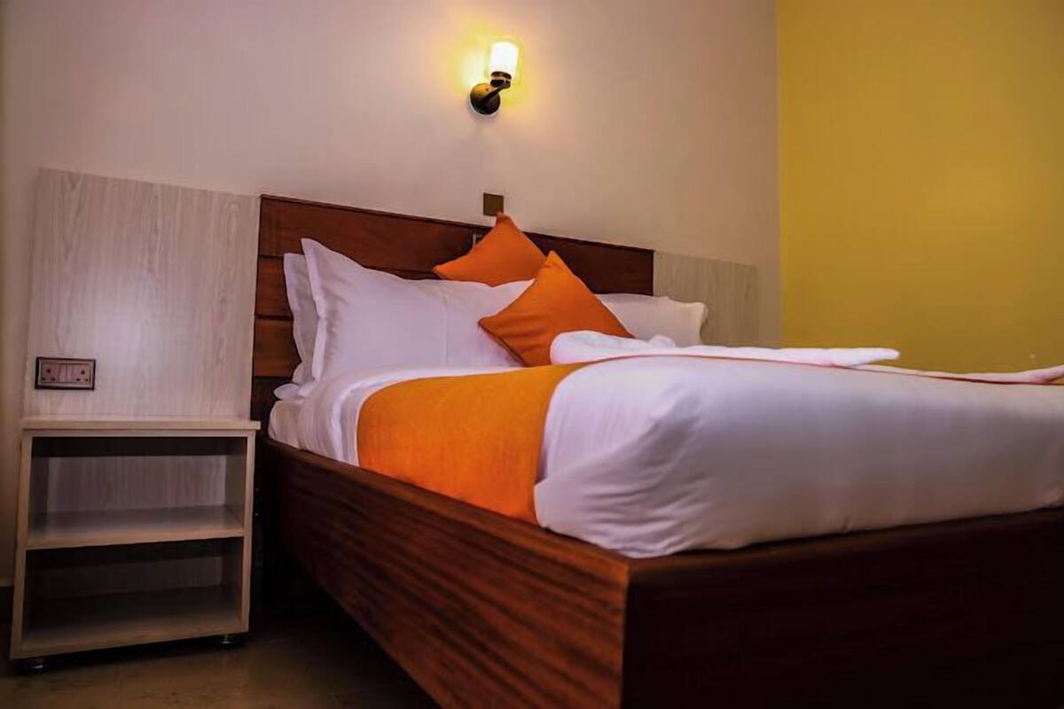 A neatly made bed with white and orange bedding, a wooden headboard, and a nightstand with a light fixture.