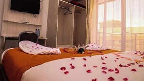 A hotel room with a bed adorned with rose petals, a TV mounted on the wall, a desk with a chair, and a wardrobe. - Sanel Hotel and Lounge Naivasha (Naivasha)