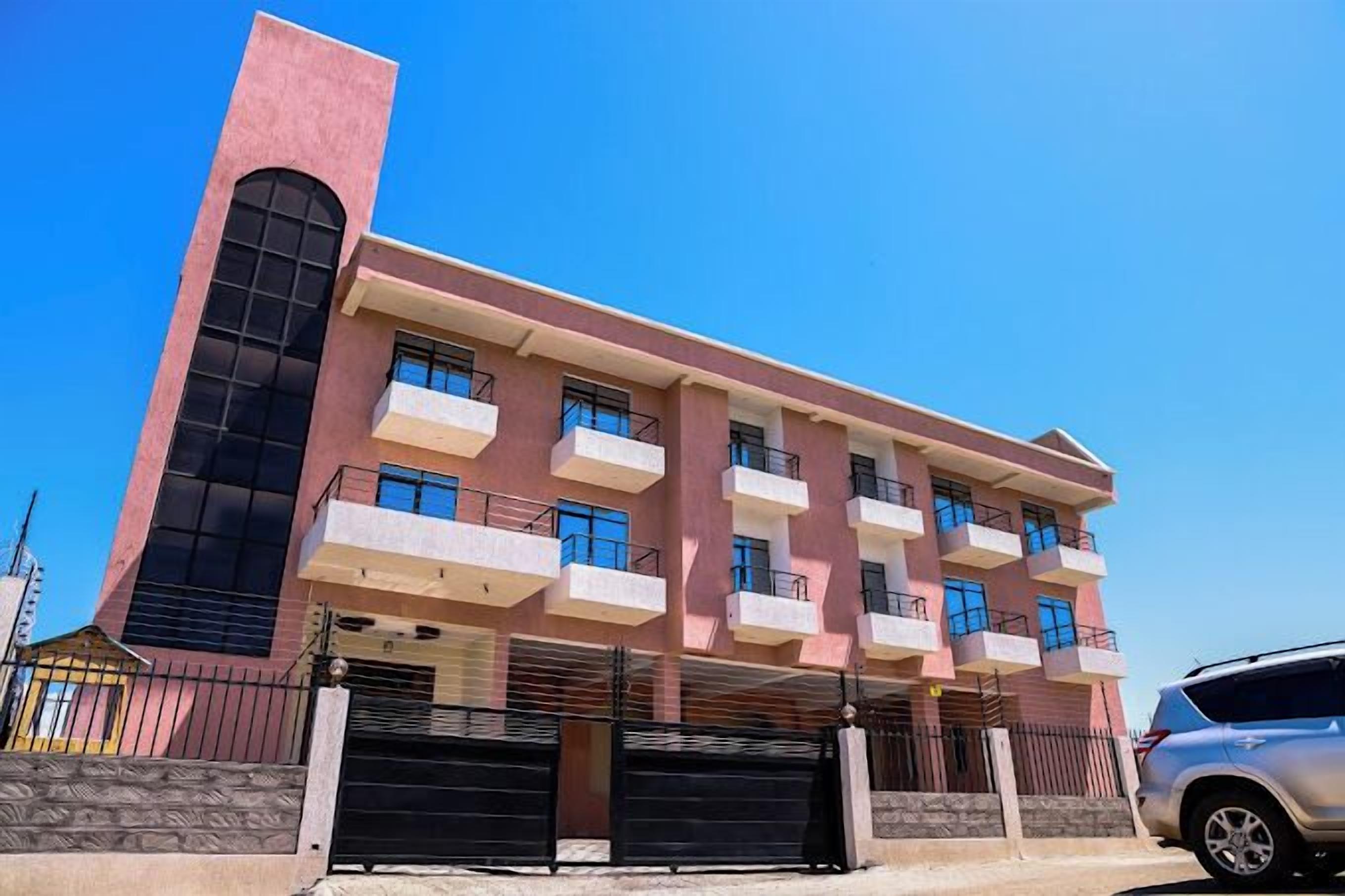 Un immeuble à plusieurs étages, doté d’une façade rose, de grandes fenêtres et d’un élément vertical bien visible sur le côté gauche.
