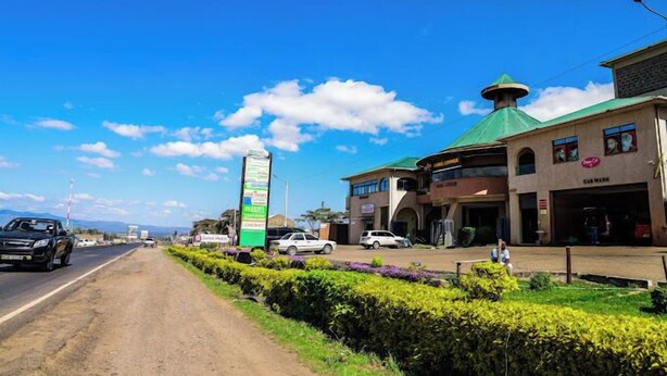 A roadside view with a signpost, a building with a green roof, and a road with vehicles. - Sanel Hotel and Lounge Naivasha (Naivasha)