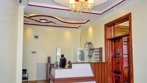 A reception area with a wooden reception desk, a glass partition, and a chandelier. - Sanel Hotel and Lounge Naivasha (Naivasha)