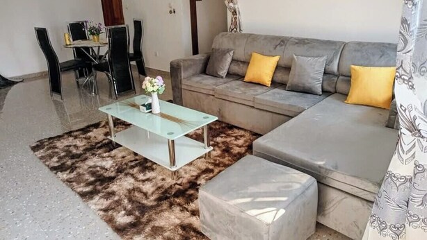 A living room with a sofa, ottoman, glass coffee table, and a dining table with chairs. - Furnished studio, Douala-Total Nkolbong close to the road and all amenities (Douala)