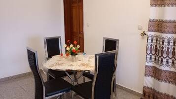 Un coin repas avec une table ronde, quatre chaises, une horloge au mur et une porte avec un rideau.