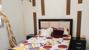 A bedroom with a bed, bedside tables, a wall-mounted air conditioner, and a window with curtains. - Furnished studio, Douala-Total Nkolbong close to the road and all amenities (Douala)
