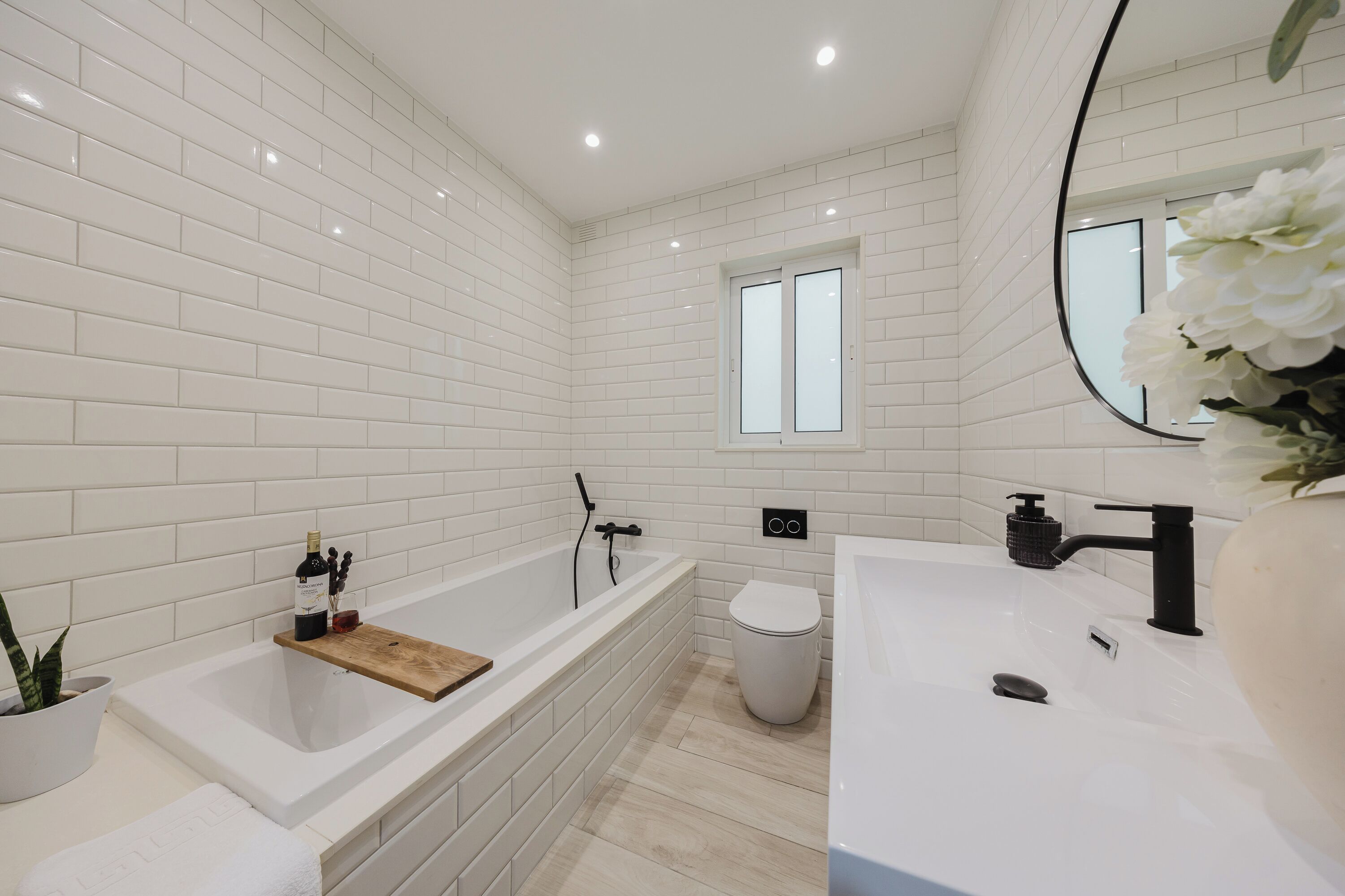 Un baño moderno con paredes de azulejos blancos, una bañera, un inodoro y un lavamanos.