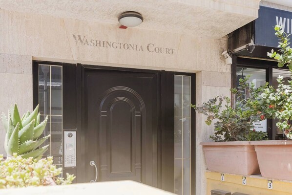 La entrada a Washingtonia Court, con una puerta de madera oscura, un cartel con el nombre y plantas en macetas al frente.