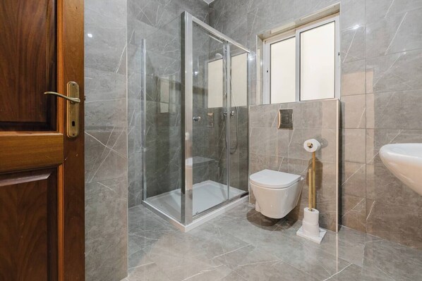 A modern bathroom with a glass-enclosed shower, a toilet, and a sink.