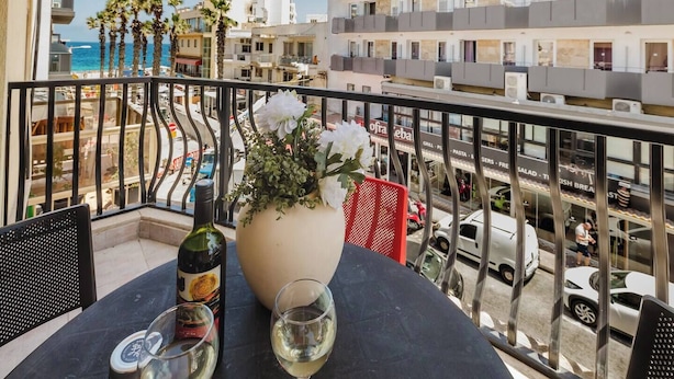 Un balcón con una mesa, una botella de vino y un jarrón de flores.