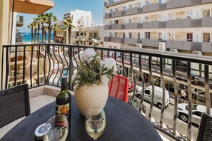 Un balcon avec une table, une bouteille de vin et un vase de fleurs.