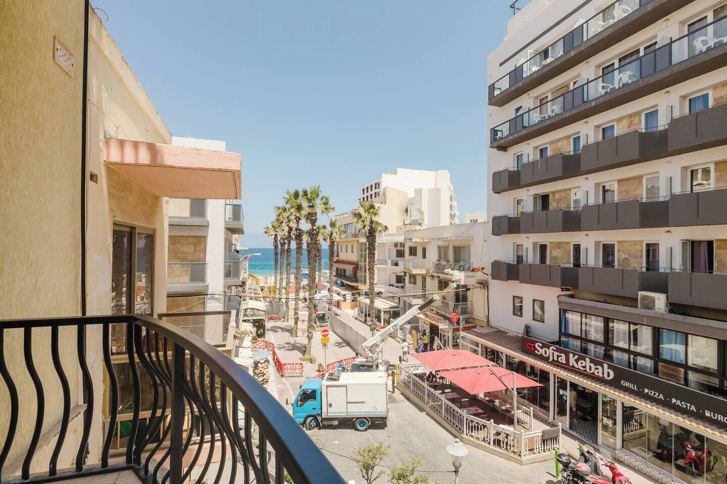 A balcony with a view of a beach, palm trees, and a restaurant named "Sofía Kebab".