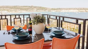 A table set for two with a view of the sea, a bottle of wine, and a vase of flowers. - Beautiful seafront apartment in Għadira Bay with 2 bedrooms, 2 bathrooms, and a large terrace offering breathtaking sea views. Located on the second floor (no lift) and just 1 minute from the sandy beach — ideal for a relaxing seaside escape. (Il-Mellieħa)