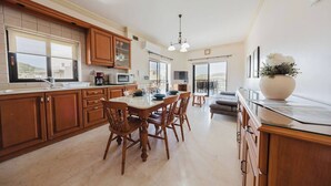 A spacious kitchen with wooden cabinets, a dining area with a table and chairs, and a large window offering a view of the outdoors.