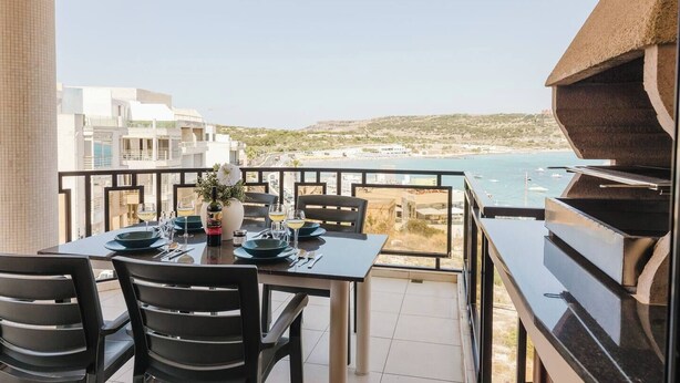 A balcony with a table set for dining, overlooking a coastal view.