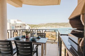 A balcony with a table set for dining, overlooking a coastal view. - Spacious seafront apartment in Għadira Bay with 3 bedrooms, 2 bathrooms, and a large terrace boasting spectacular sea views. Located on the third floor (no lift) and only 1 minute from the sandy beach — perfect for up to 5 guests. (Il-Mellieħa)