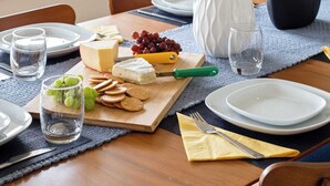 Une table à manger dressée avec des assiettes, un vase, une plante en pot et une planche à fromage accompagnée de raisins et de crackers.