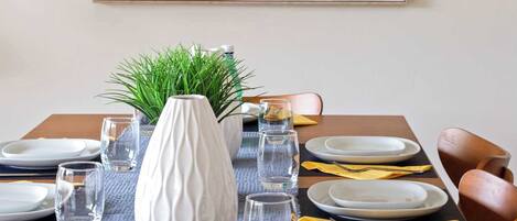 Una mesa de comedor dispuesta con platos, vasos, un florero y una tabla de quesos.