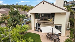 Une maison à deux étages avec un balcon, une terrasse dotée d’une table et de chaises, et un jardin bien entretenu.