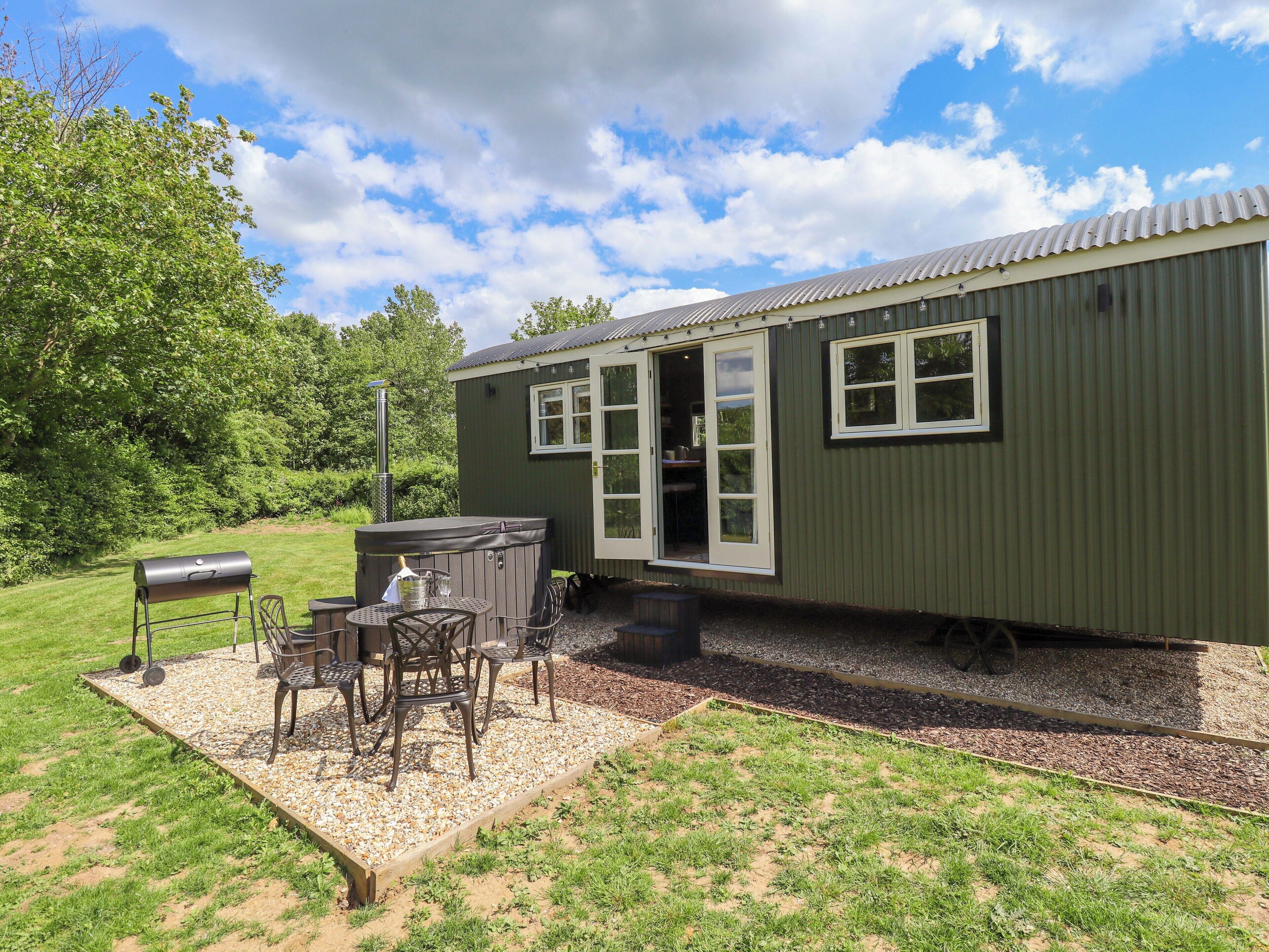 A small, single-story structure with a patio area featuring a grill, seating, and a hot tub.