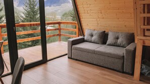 Une pièce chaleureuse avec un plancher en bois, un canapé gris agrémenté de coussins et une grande fenêtre donnant sur une vue imprenable sur les montagnes.