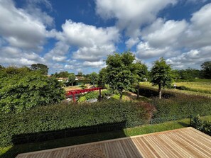 Una terraza de madera con vistas a un jardín ajardinado, con setos y árboles.