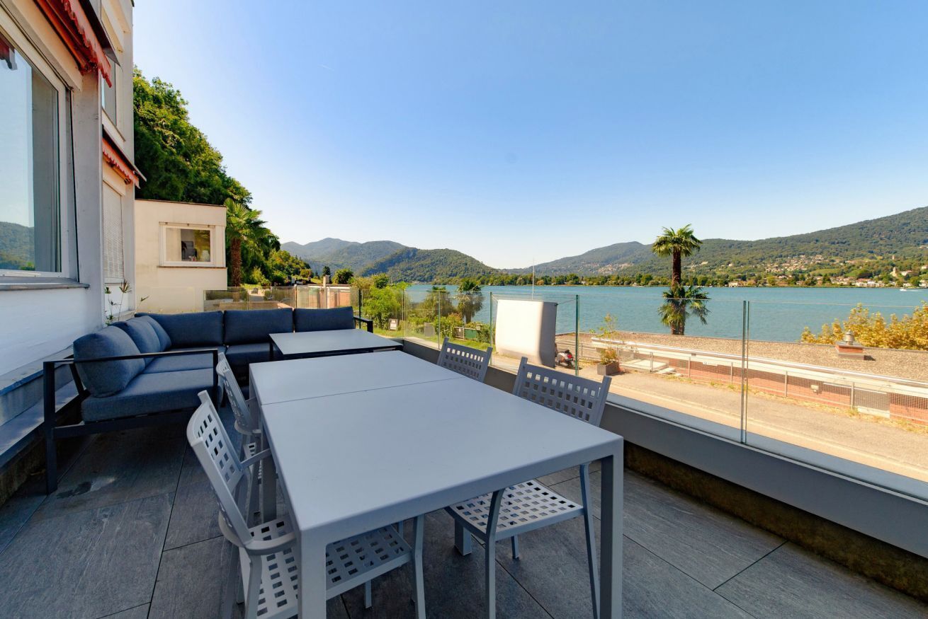 Eine Terrasse mit Tisch und Stühlen, einer Sitzecke und Blick auf See und Berge.