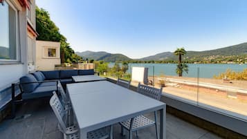 Eine Terrasse mit Tisch und Stühlen, einer Sitzecke und Blick auf See und Berge.