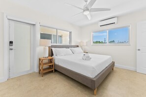 Un dormitorio con cama, mesita de noche, ventilador de techo, equipo de aire acondicionado y ventana con vistas.