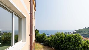 Un balcón con vista al mar, cielo despejado y un jardín bien cuidado.