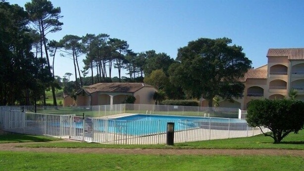 A swimming pool surrounded by a white fence, with a building in the background.