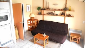 A compact living space with a sofa, a small wooden table, a lamp, and a shelf with decorative items.
