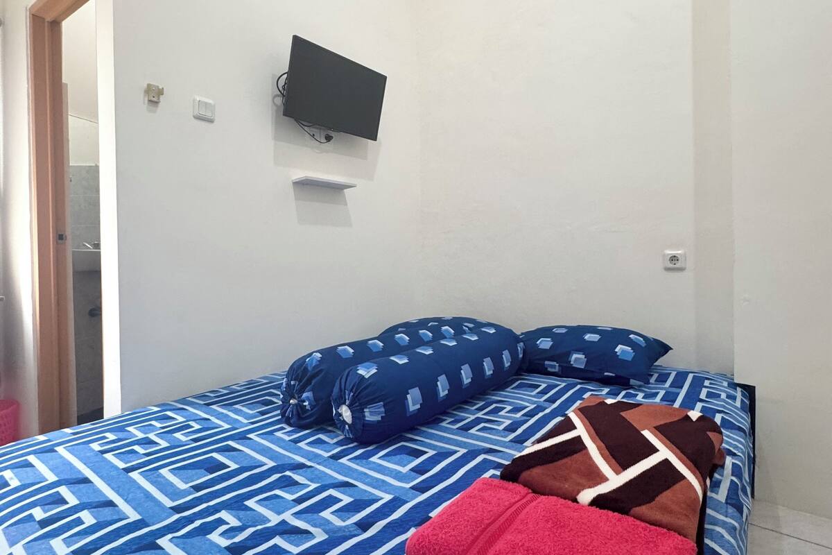 Un dormitorio con una cama, un televisor de pantalla plana montado en la pared y una puerta que da a otra habitación.