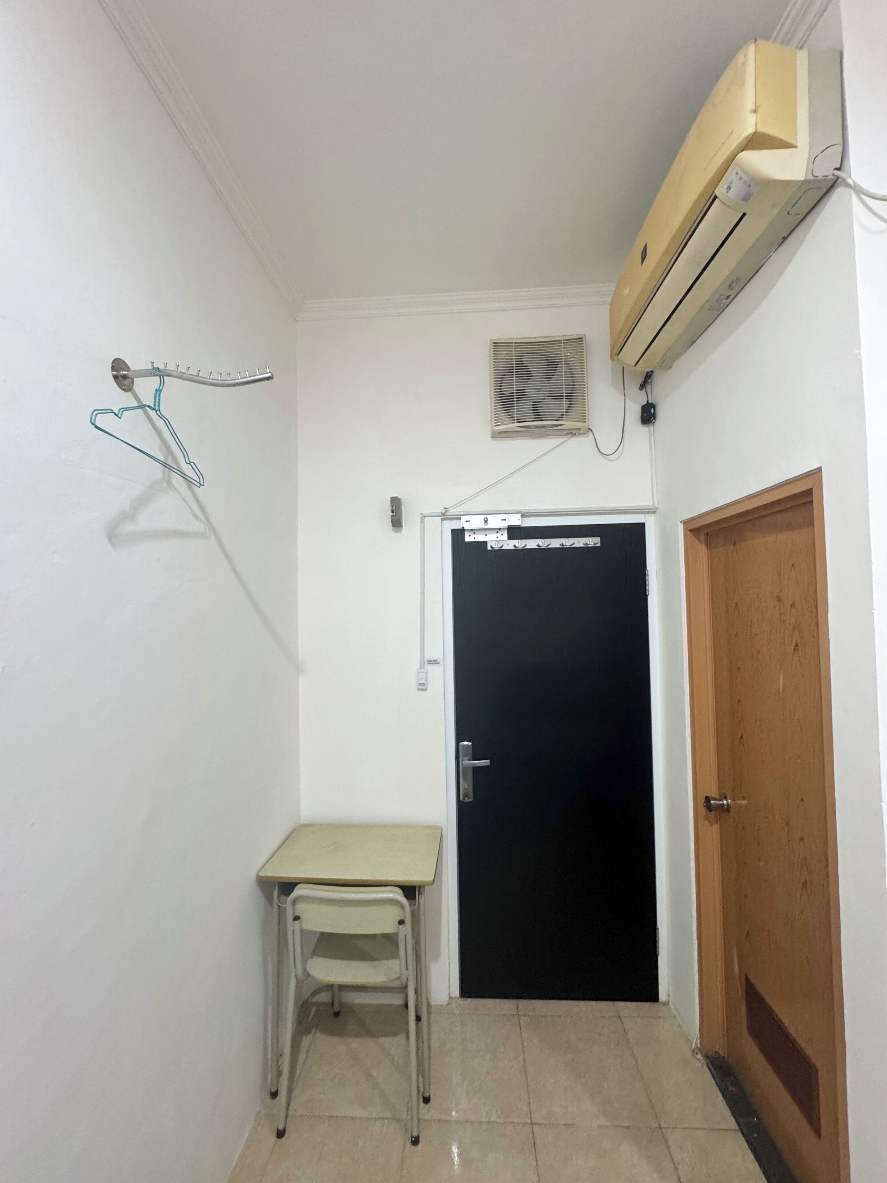 Una habitación pequeña con una puerta, una mesa, una silla, un equipo de aire acondicionado y un calentador de pared.