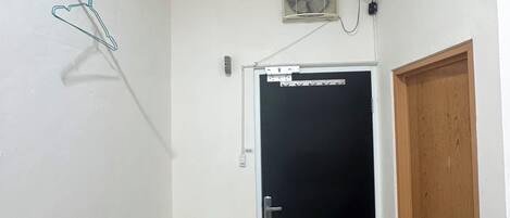 Una habitación pequeña con una puerta, una mesa, una silla, un equipo de aire acondicionado y un calentador de pared.