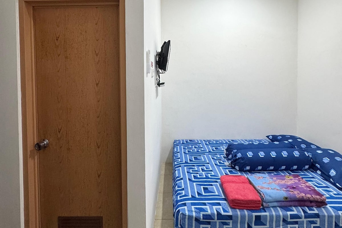 Una habitación con puerta de madera, cama con ropa de cama estampada y lámpara fijada en la pared.