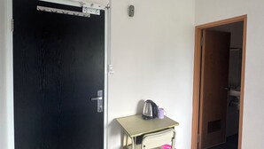Une pièce avec une porte noire, une petite table sur laquelle se trouvent une bouilloire et une tasse, et un appareil de climatisation fixé au mur.