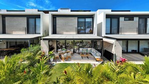 A modern two-story house with a covered patio area featuring outdoor furniture and a dining table. - Vista Natura 54 | Beach Access | Rooftop Deck | Gated Community | Pool & Hot Tub (Nuevo Vallarta)