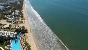 An aerial view of a coastal resort with a long beachfront, a swimming pool, and several buildings. - Vista Natura 54 | Beach Access | Rooftop Deck | Gated Community | Pool & Hot Tub (Nuevo Vallarta)