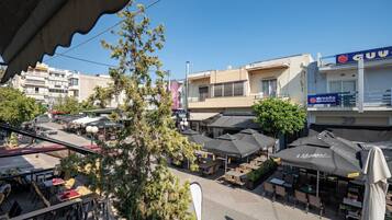 Café al aire libre con mesas y sombrillas, rodeado de edificios y árboles.