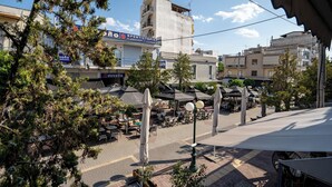 Un espace de café en plein air, avec des tables et des parasols, entouré d’arbres et d’immeubles.