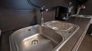 Un évier de cuisine en acier inoxydable, doté d’un robinet moderne, d’une machine à café et d’un porte-ustensiles placé sur le plan de travail.