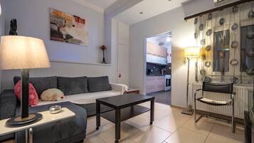 Sala de estar con sofá, mesa de centro y lámpara. Se observa una cocina al fondo.