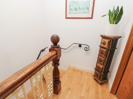 A wooden staircase with a handrail, a white wall with a framed painting, and a potted plant on a wooden cabinet.