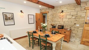 A dining area with a wooden table and chairs, a stone wall, and a kitchen area with a microwave and a kettle. - Hivewood Cottage (Keighley)