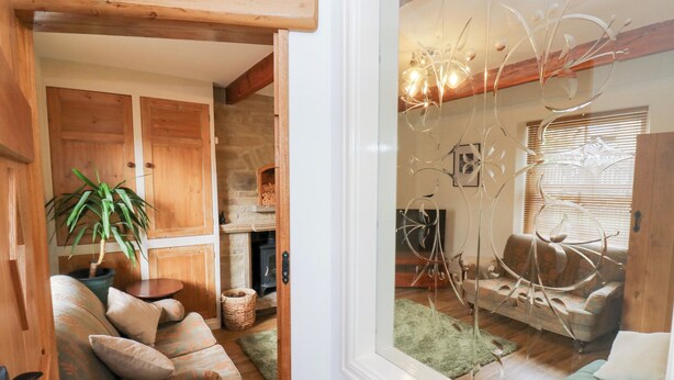 A cozy living room with a wooden sofa, a green armchair, and a fireplace. - Hivewood Cottage (Keighley)