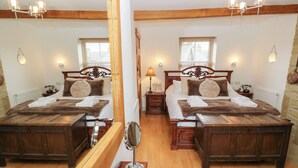 A mirrored room with two wooden beds, a mirror, a lamp, and a wooden chest. - Hivewood Cottage (Keighley)