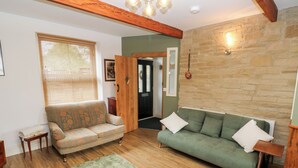 A living room with two sofas, a wooden floor, a green rug, and a stone wall. - Hivewood Cottage (Keighley)